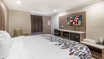 A hotel room with a large bed, a desk with a computer, a television, and a minibar.