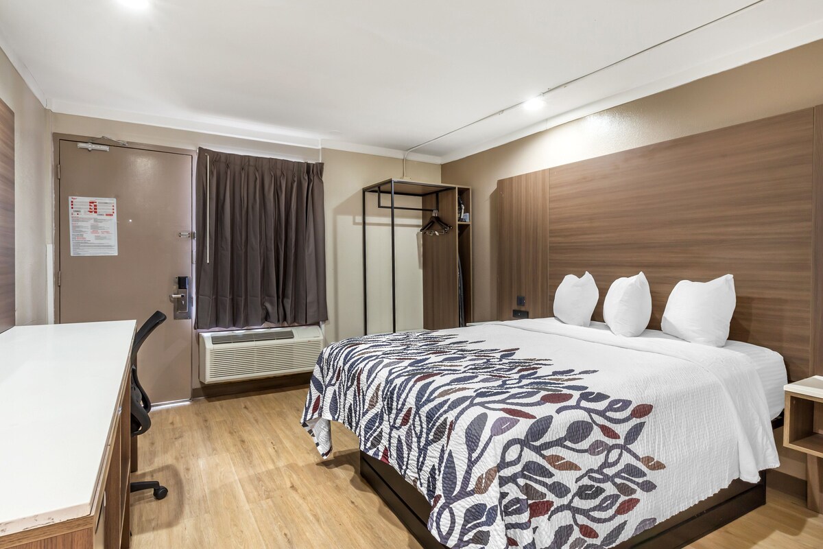 Ein Hotelzimmer mit Bett, Schreibtisch, Stuhl, Kleiderschrank und einem Fenster mit Vorhängen.