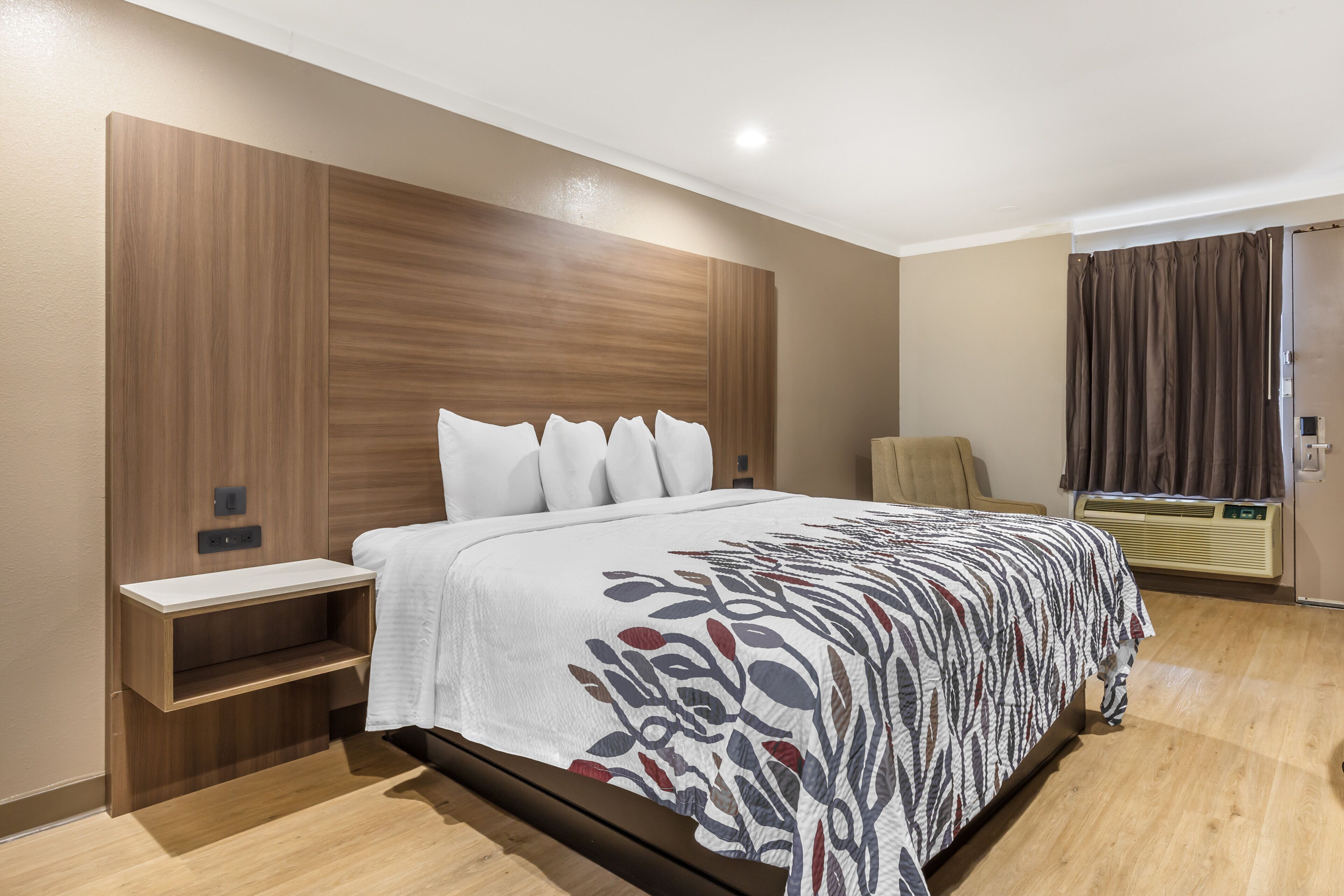 A hotel room with a large bed, a bedside table, a wardrobe, a heater, and a window with curtains.