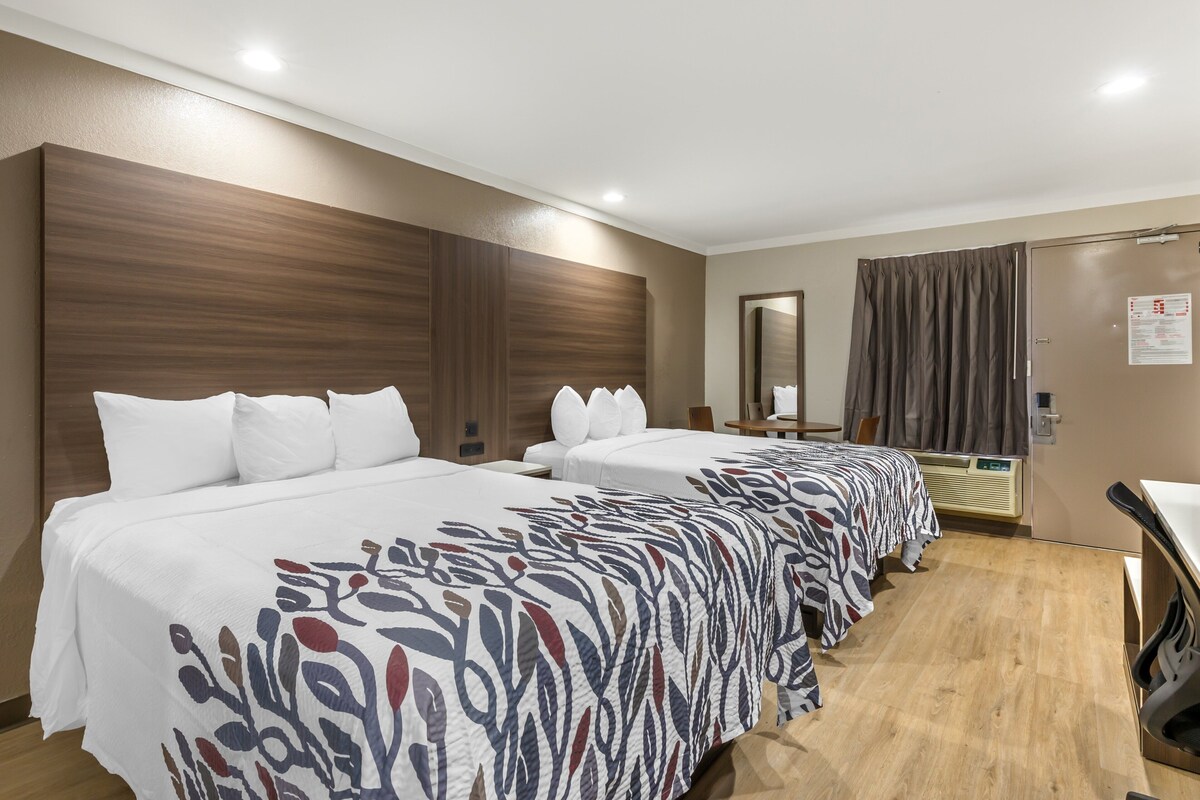 Ein Hotelzimmer mit zwei Betten, einem hölzernen Kopfteil, einem Spiegel, einem Schreibtisch und einem Vorhangfenster.