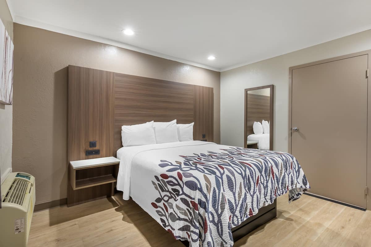 A hotel room with a large bed, a wooden headboard, a bedside table, and a wardrobe.