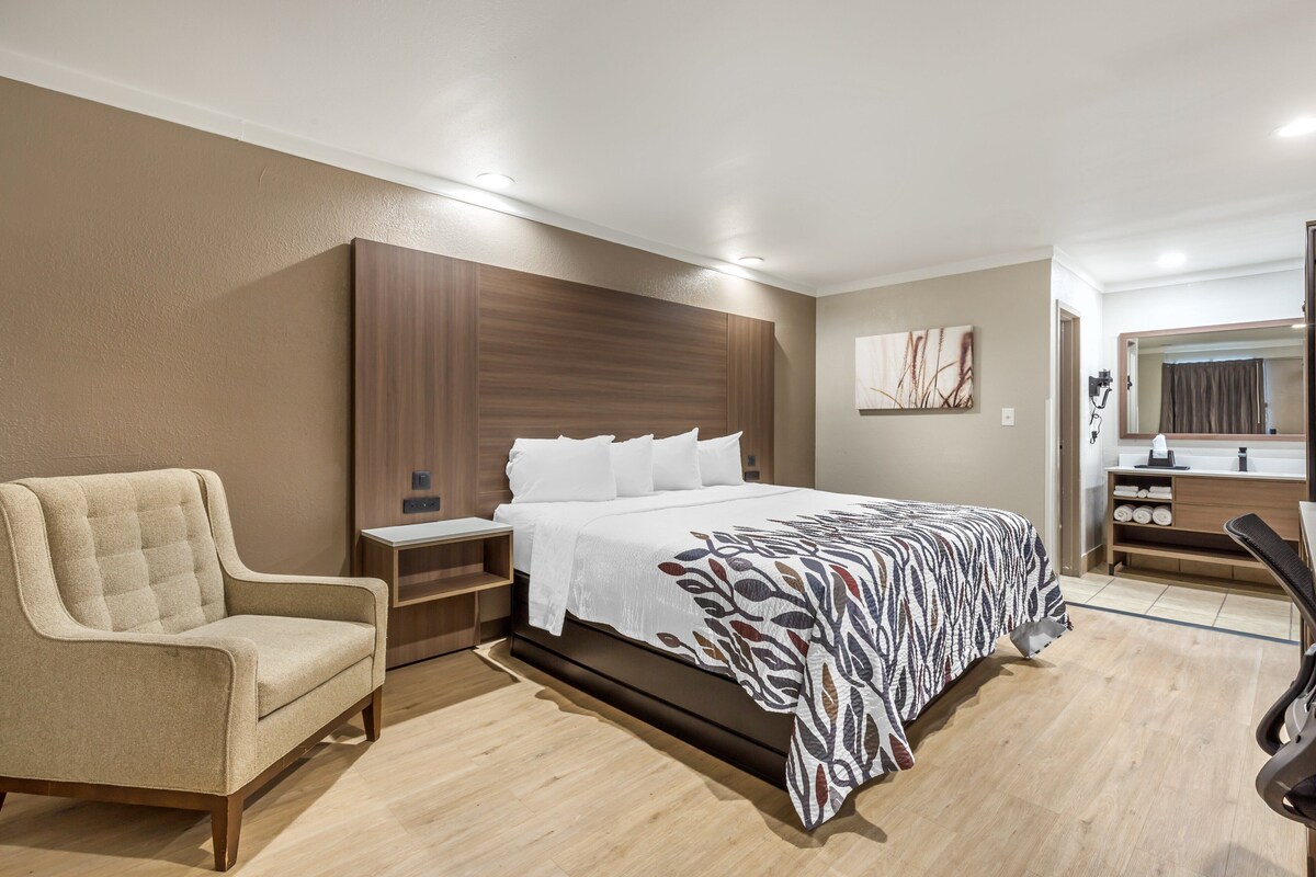 Ein modernes Hotelzimmer mit einem großen Bett, einer Sitzecke, einem Schreibtisch und einem Badezimmerspiegel.