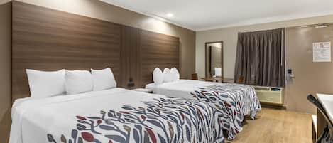 Une chambre d’hôtel avec deux lits, une tête de lit en bois, un miroir, un bureau et une fenêtre avec des rideaux.