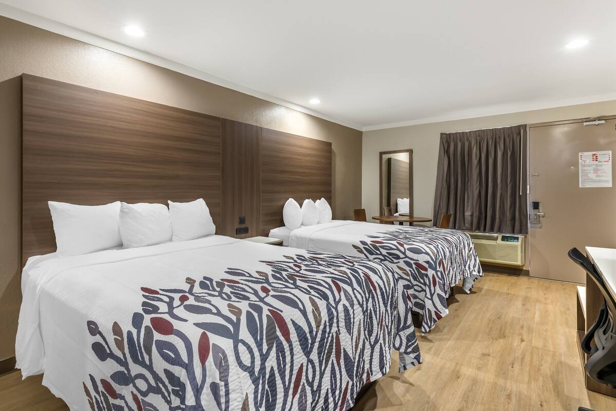A hotel room with two beds, a wooden headboard, a mirror, a desk, and a window with curtains.