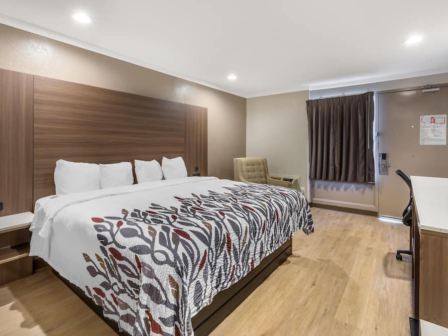A hotel room with a large bed, a desk, a chair, and a sliding door.