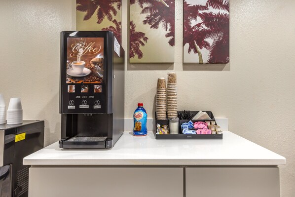 Eine Kaffeemaschine mit Kaffeetassen, eine Kaffeemilch-Flasche sowie ein Tablett mit Einwegbechern und Besteck auf einer Theke.