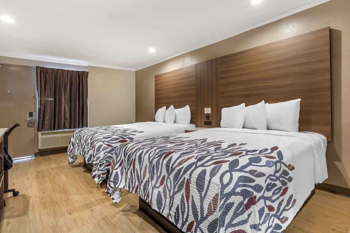 Ein Hotelzimmer mit zwei Betten, einem Schreibtisch und einem Fenster mit Vorhängen.