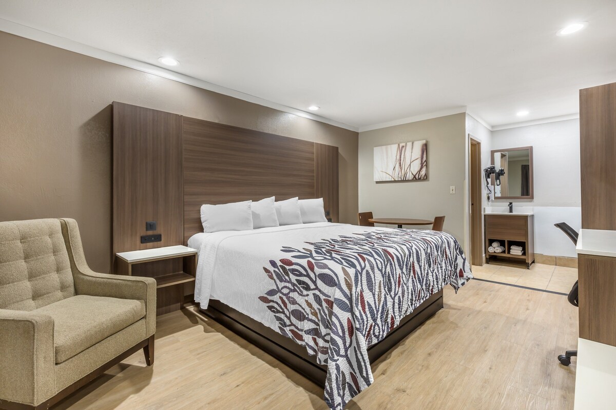 Ein modernes Hotelzimmer mit einem großen Bett, einer Couch, einem Schreibtisch und einem Badezimmer mit Spiegel und Waschbecken.
