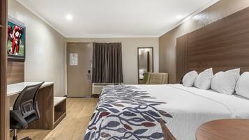 A hotel room with a bed, a desk, a chair, a mirror, and a television.