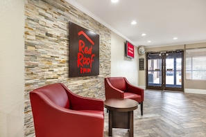 A Red Roof Inn lobby with stone wall decor, red leather chairs, a small wooden table, and a sign indicating free Wi-Fi in all rooms. - Red Roof Inn Raleigh Northeast - Downtown (Raleigh)
