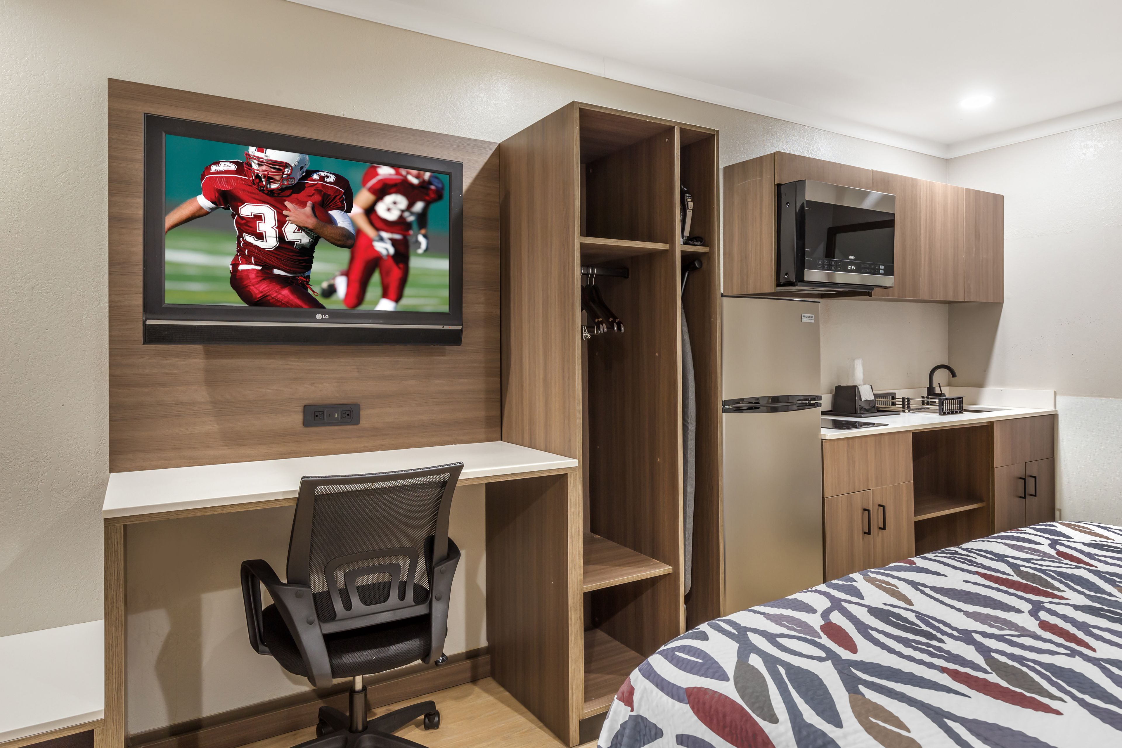 Une chambre d’hôtel comprenant un lit, un bureau avec une chaise, un téléviseur fixé au mur, un four à micro-ondes et une petite kitchenette.