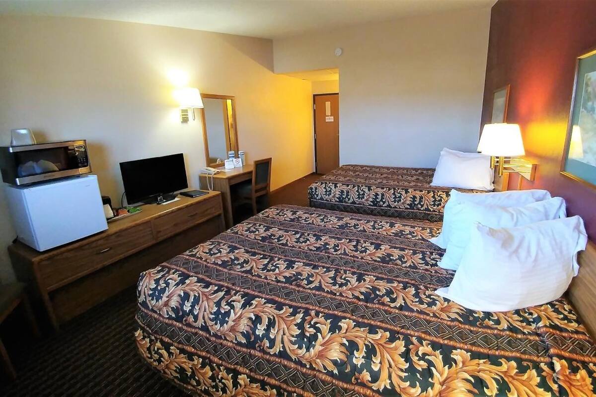 A hotel room with two beds, a desk with a TV, a refrigerator, and a painting on the wall.