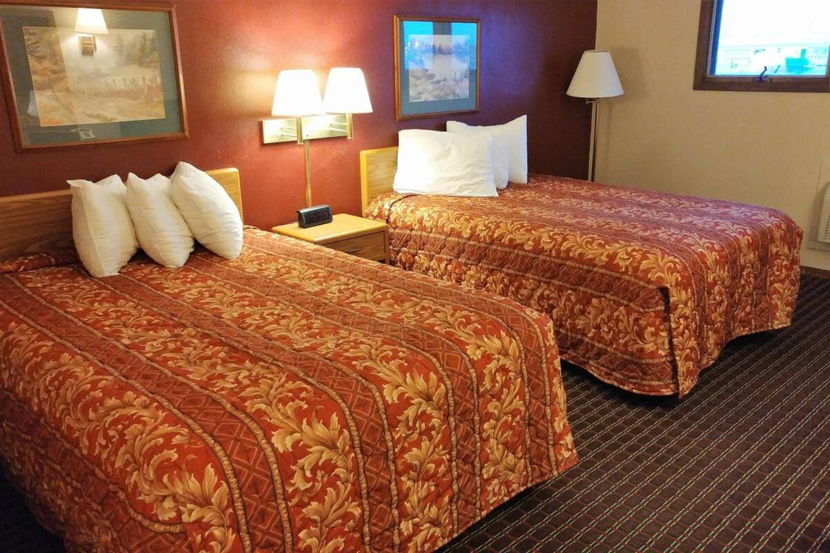 A hotel room with two beds, each with a patterned bedspread, a nightstand with a lamp, and framed pictures on the walls.