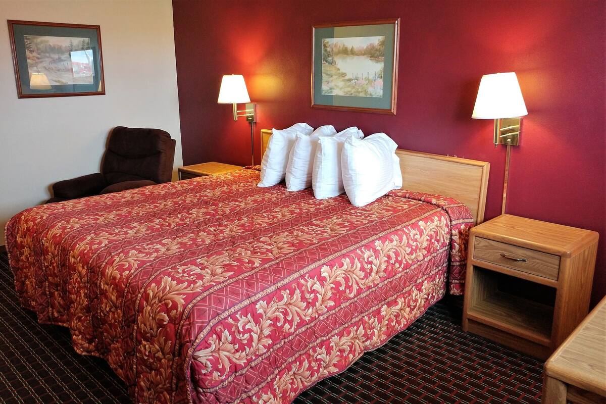 A hotel room with a large bed, two bedside tables, a chair, and two wall-mounted lamps.