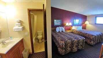 Ein Hotelzimmer mit Bad, einem Bett mit floralem Bettbezug, einem Nachttisch und einer Lampe.