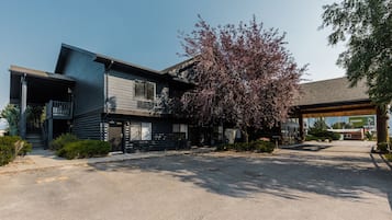 A two-story building with a covered outdoor area, a parking lot, and a tree with purple leaves.