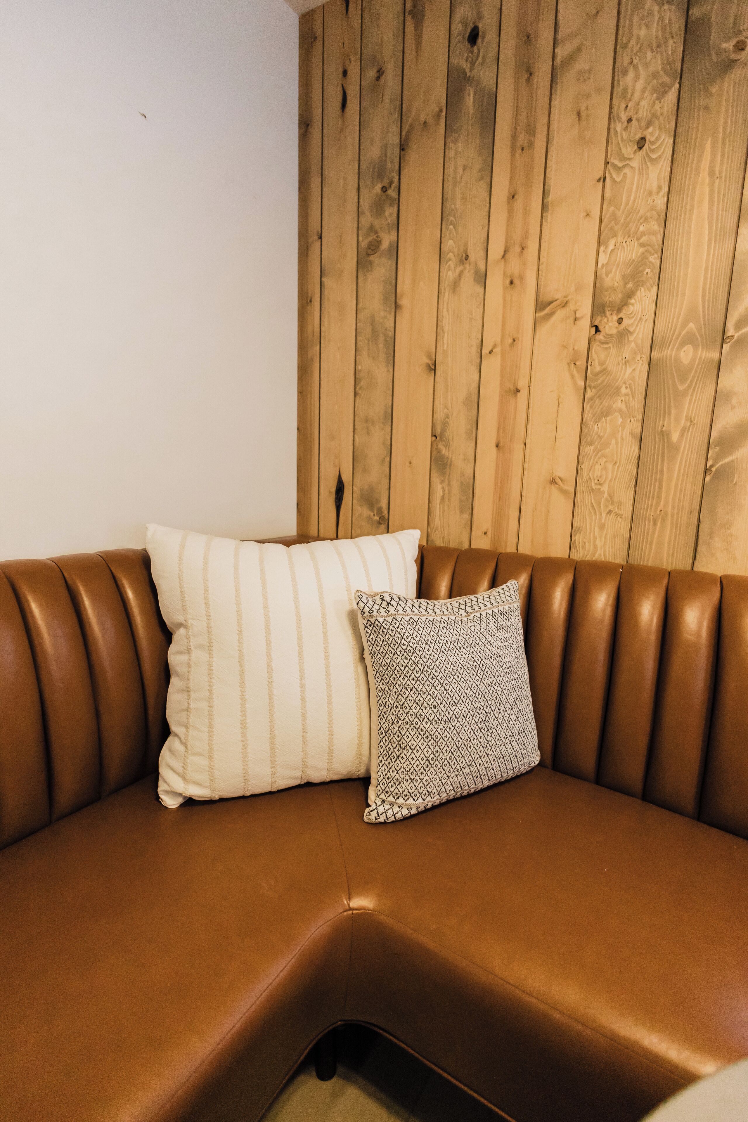 Un canapé en cuir marron avec deux coussins, adossé à un mur en bois.
