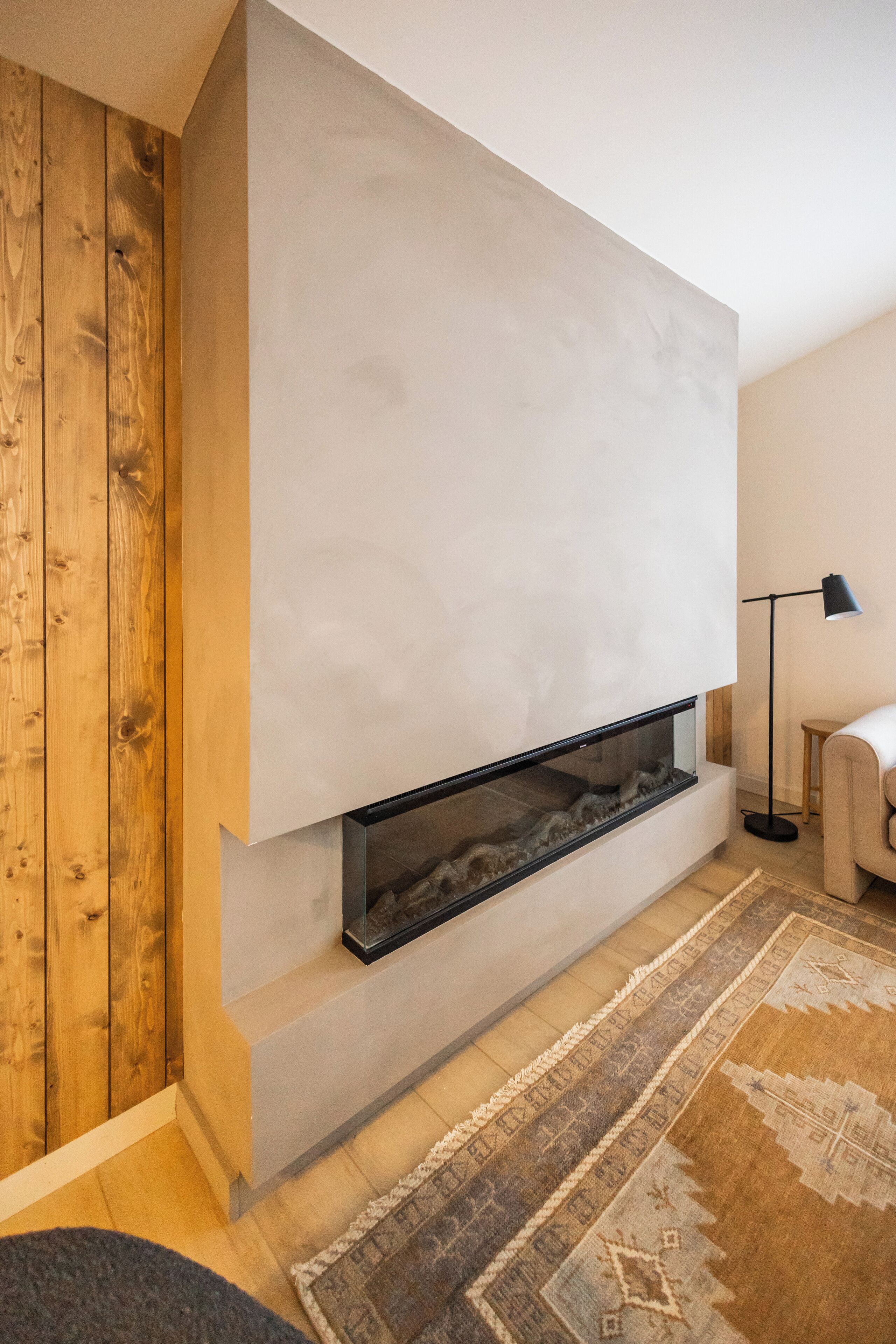 A modern living room with a built-in fireplace, wooden paneling on one wall, a patterned rug, and a floor lamp.
