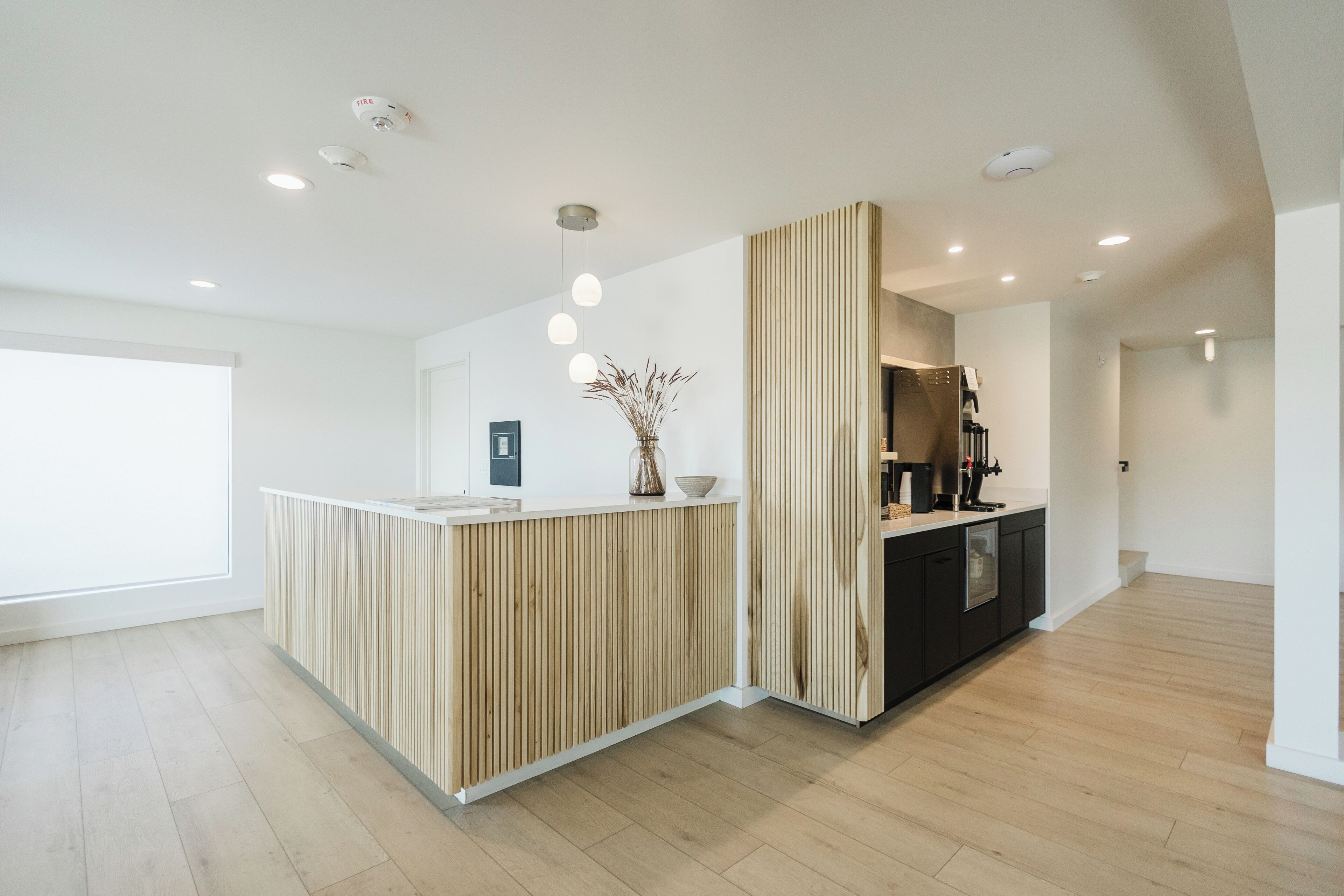 A modern reception area with a wooden reception desk, a vase with dried plants, and a coffee machine.