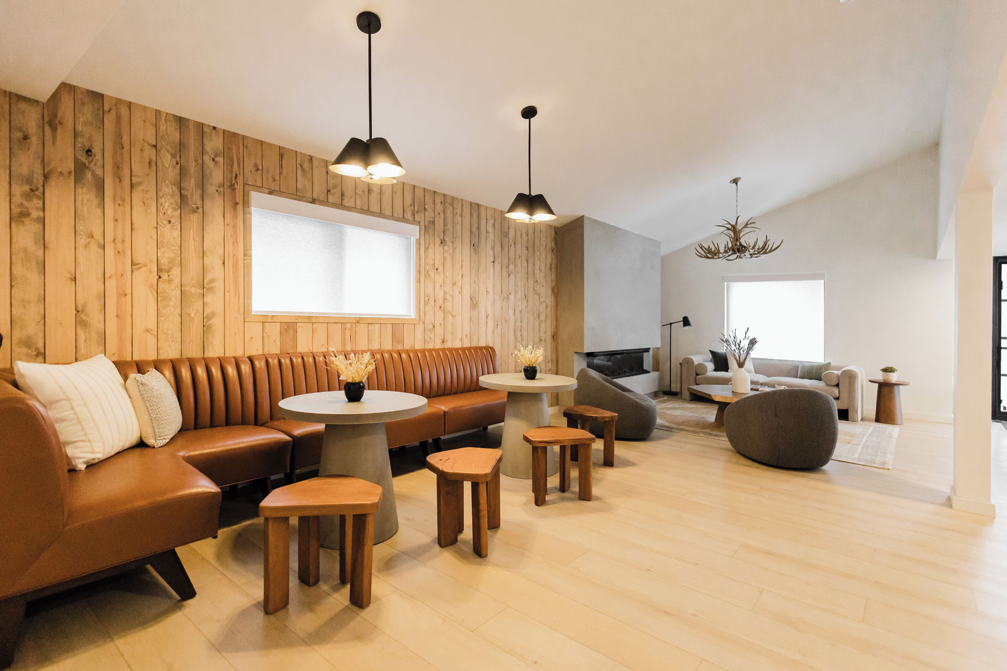 A modern living room with a wooden wall, a brown leather sofa, round wooden tables, and a large window.
