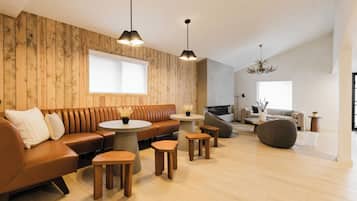 A modern living room with a wooden wall, a brown leather sofa, round wooden tables, and a large window.