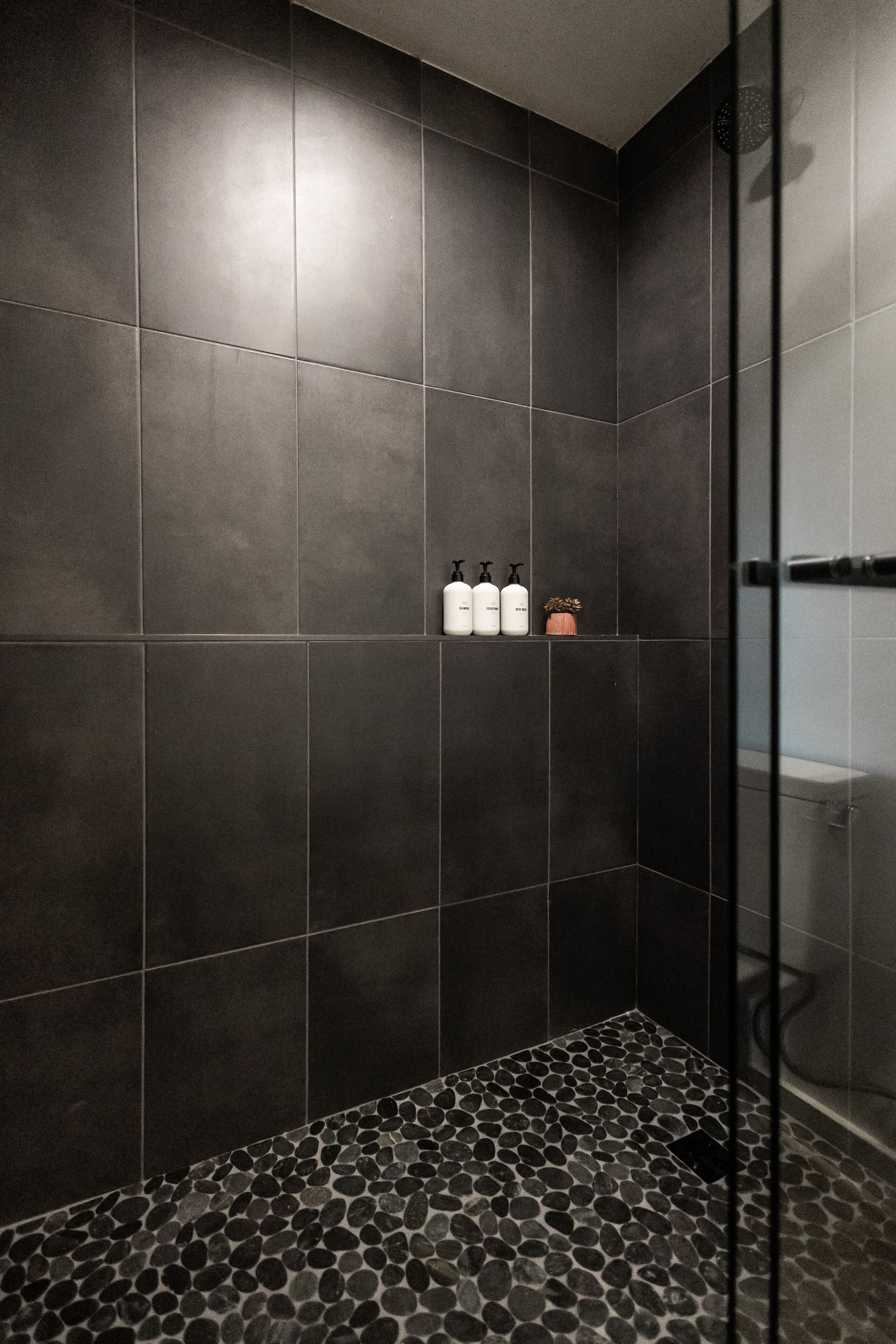 A shower area with dark tiles and a pebble-patterned floor.