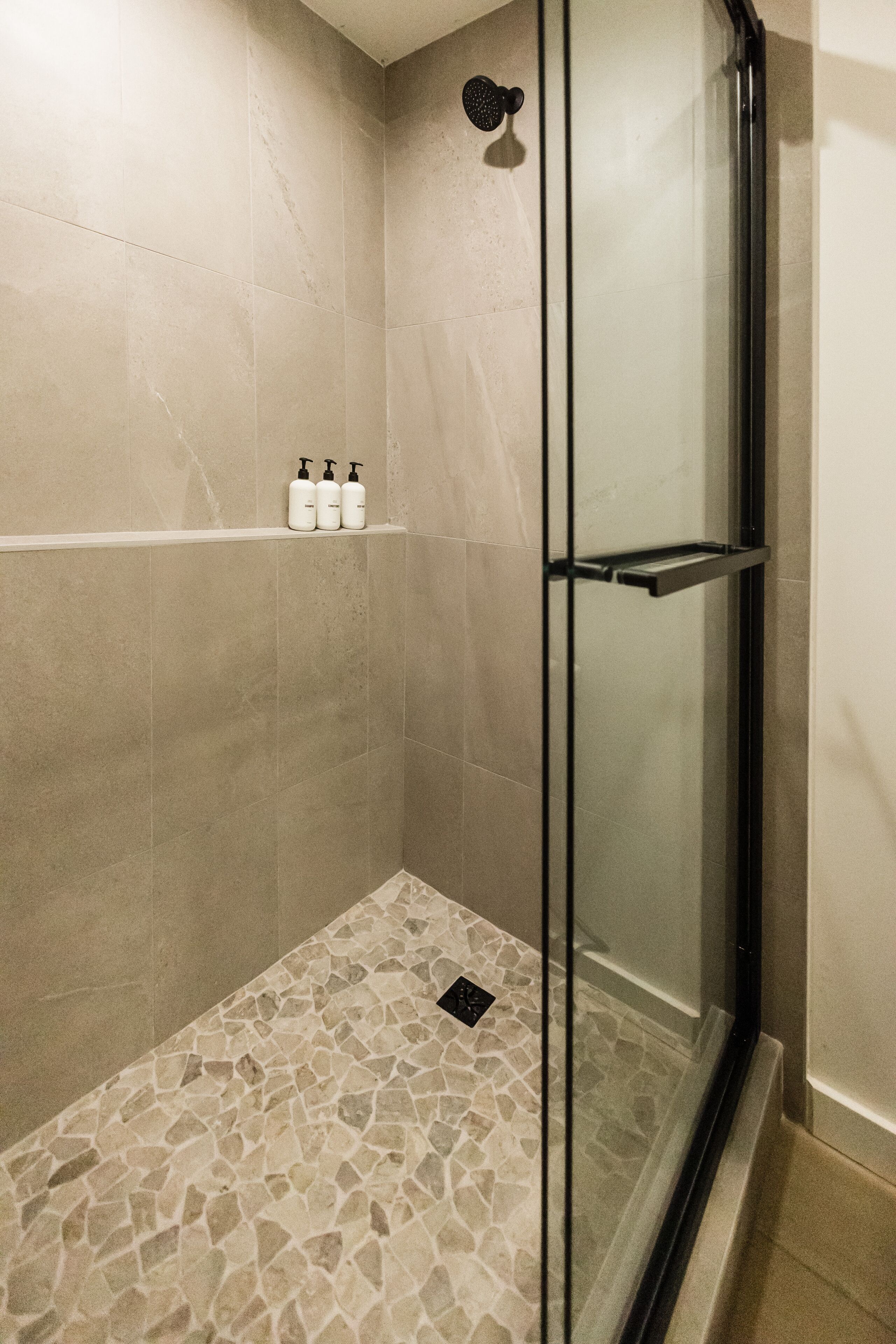 A shower area with a glass door, beige tiled walls, and a mosaic floor.