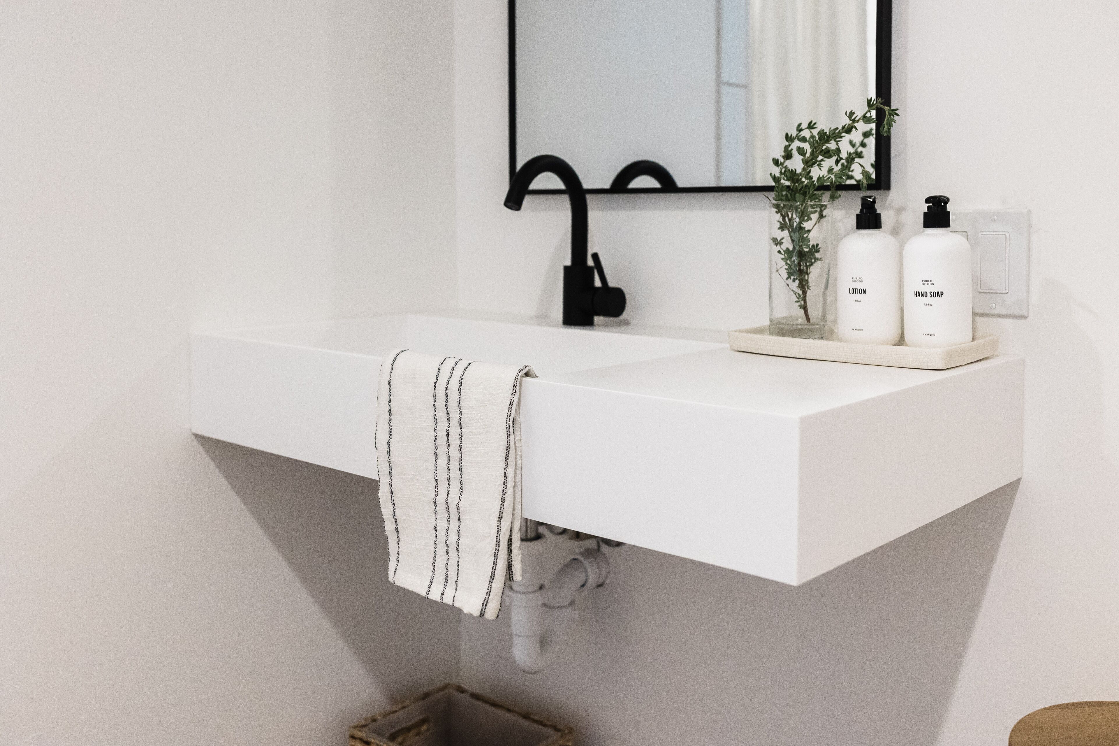A white bathroom sink with a black faucet, a towel hanging on the side, and two bottles of lotion and hand soap on the countertop.