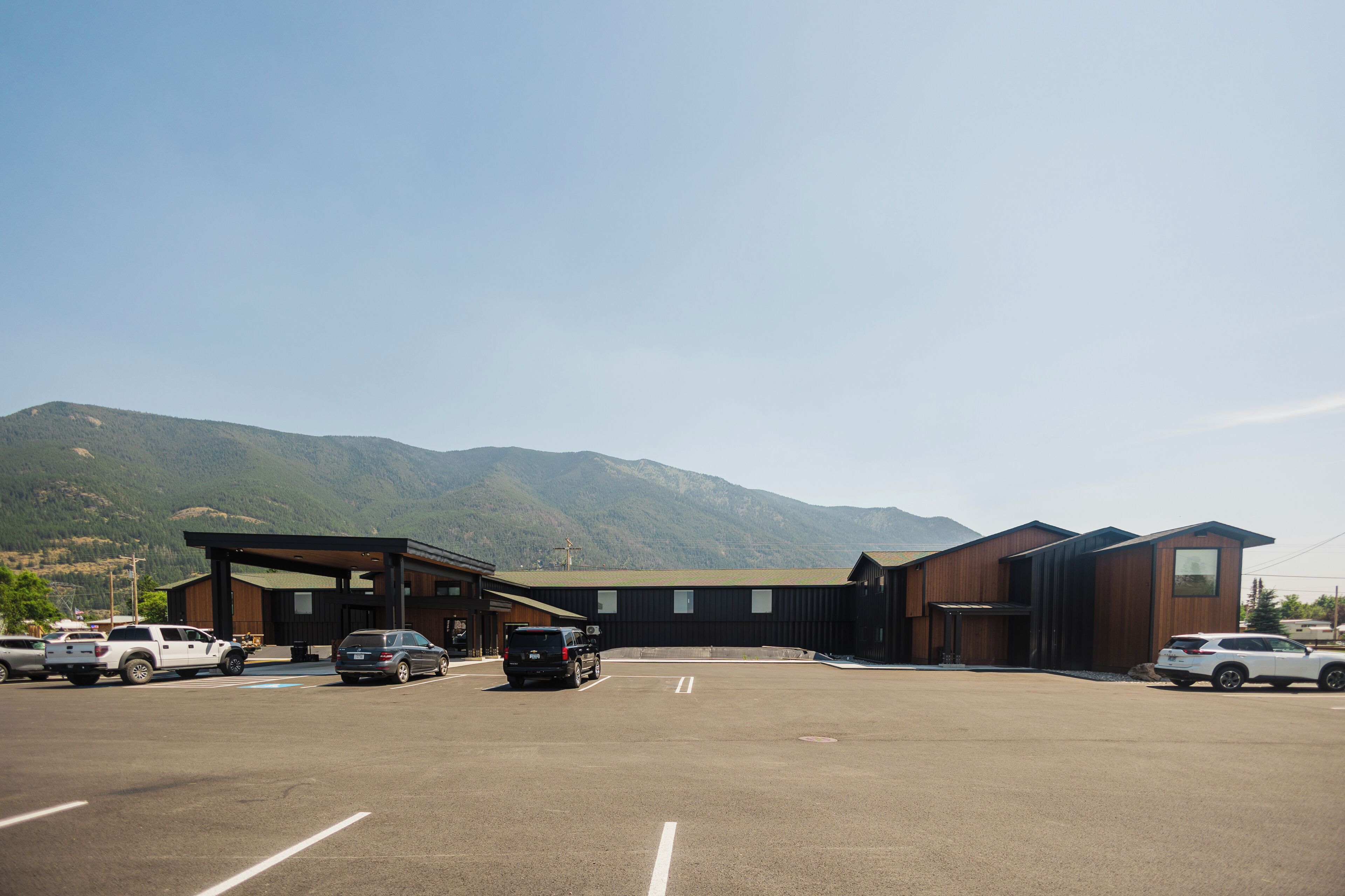 A parking lot with several cars, a building with a modern design, and mountains in the background.