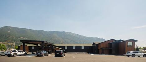 A parking lot with several cars, a building with a modern design, and mountains in the background.