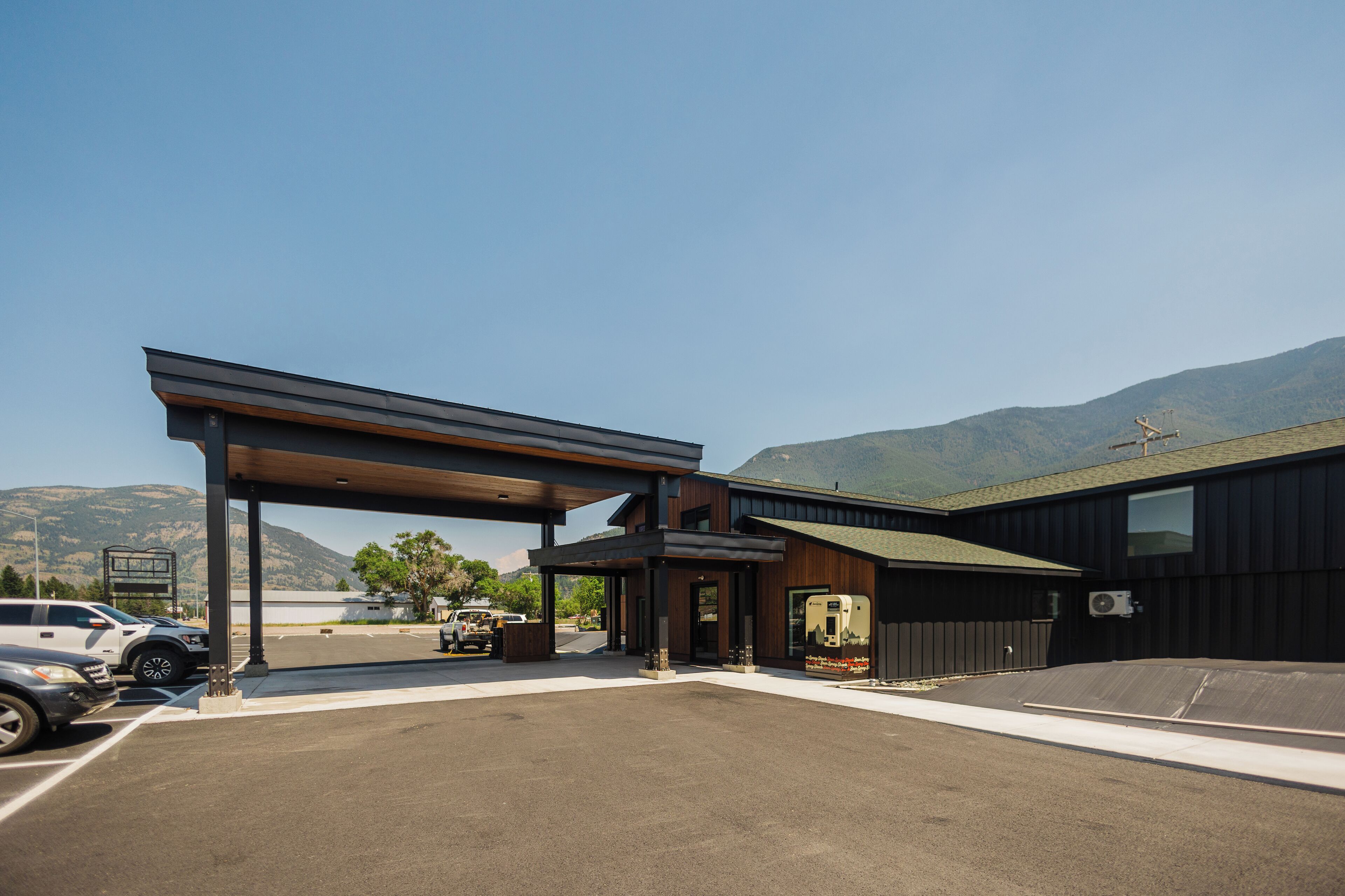 A modern building with a covered parking area and a view of mountains in the background.