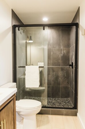 A modern bathroom with a glass-enclosed shower, a white toilet, and a tiled floor.