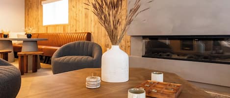 Una sala de estar moderna con una mesa de centro de madera, un jarrón blanco con plantas secas y una chimenea.