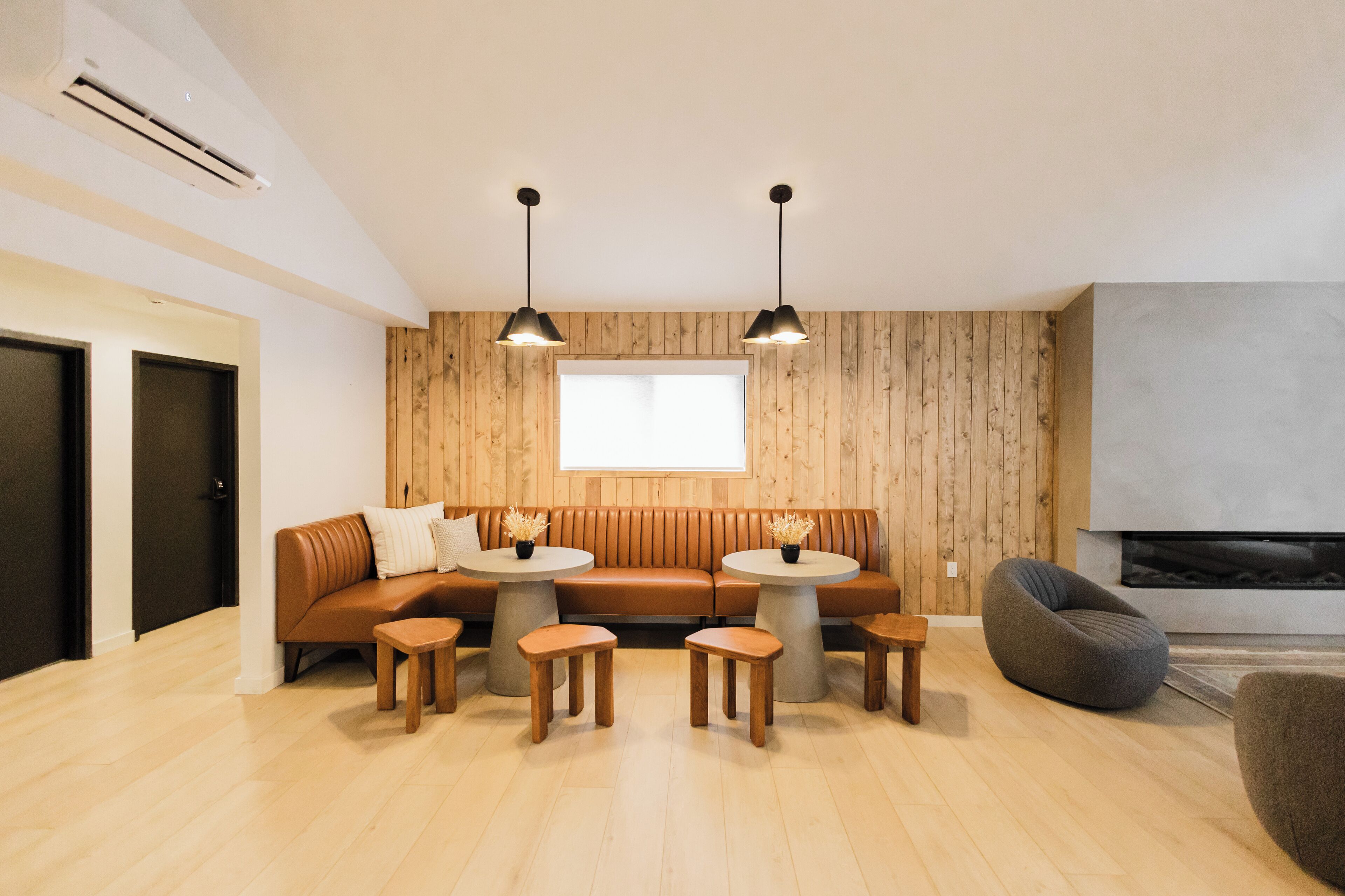 A modern living room with a brown leather sofa, two round wooden tables, and a gray bean bag.