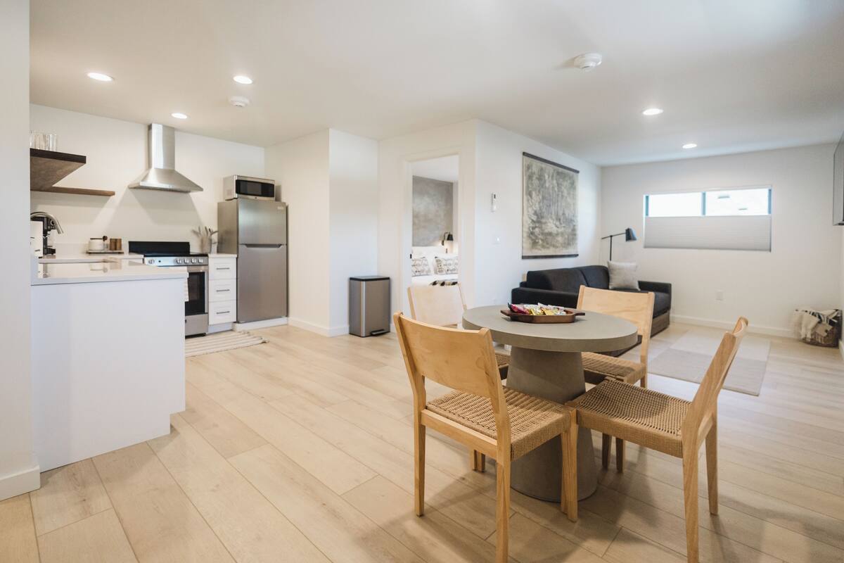 A modern kitchen with white cabinetry, stainless steel appliances, and a dining area with a round table and wooden chairs.