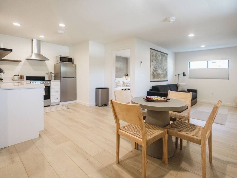 A modern kitchen with white cabinetry, stainless steel appliances, and a dining area with a round table and wooden chairs.