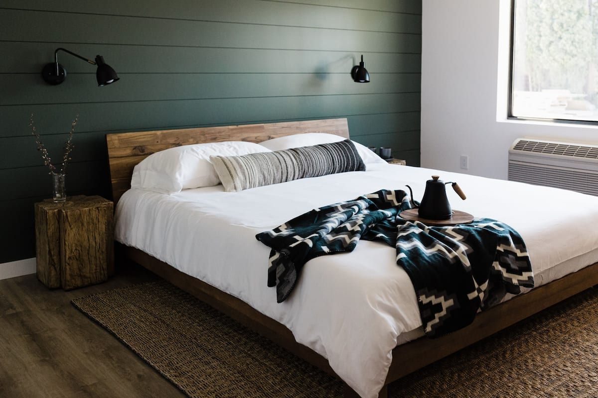 A neatly made bed with a wooden headboard, a patterned throw blanket, and a bedside table with a lamp.