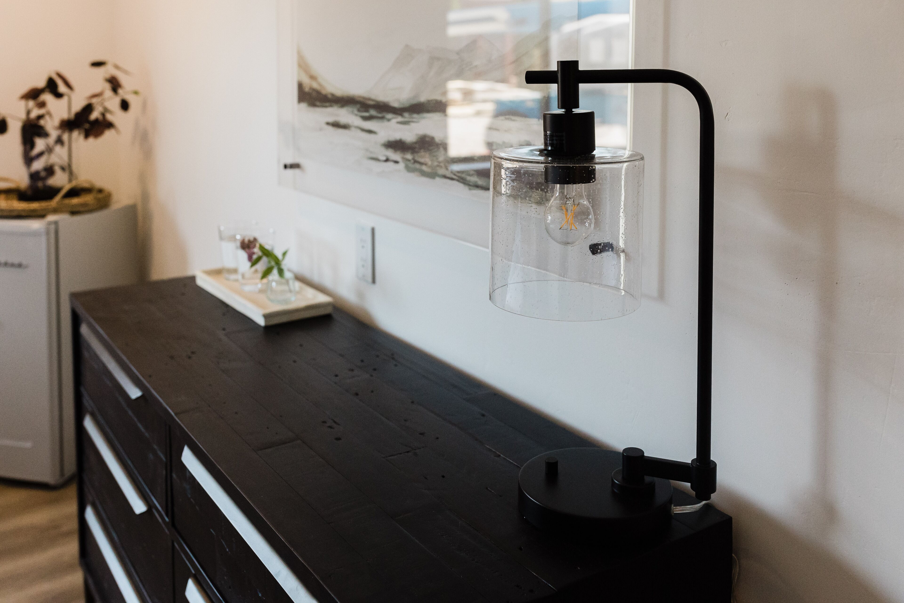 A modern room with a dark wooden dresser, a clear glass bottle with a pump, and a framed artwork on the wall.