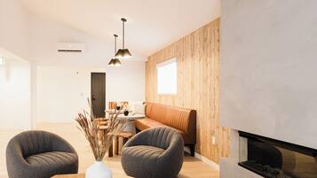 A modern living room with a wooden dining table, two armchairs, a chandelier, and a fireplace.