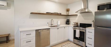 A modern kitchen with white cabinetry, stainless steel appliances, and a wooden bench.