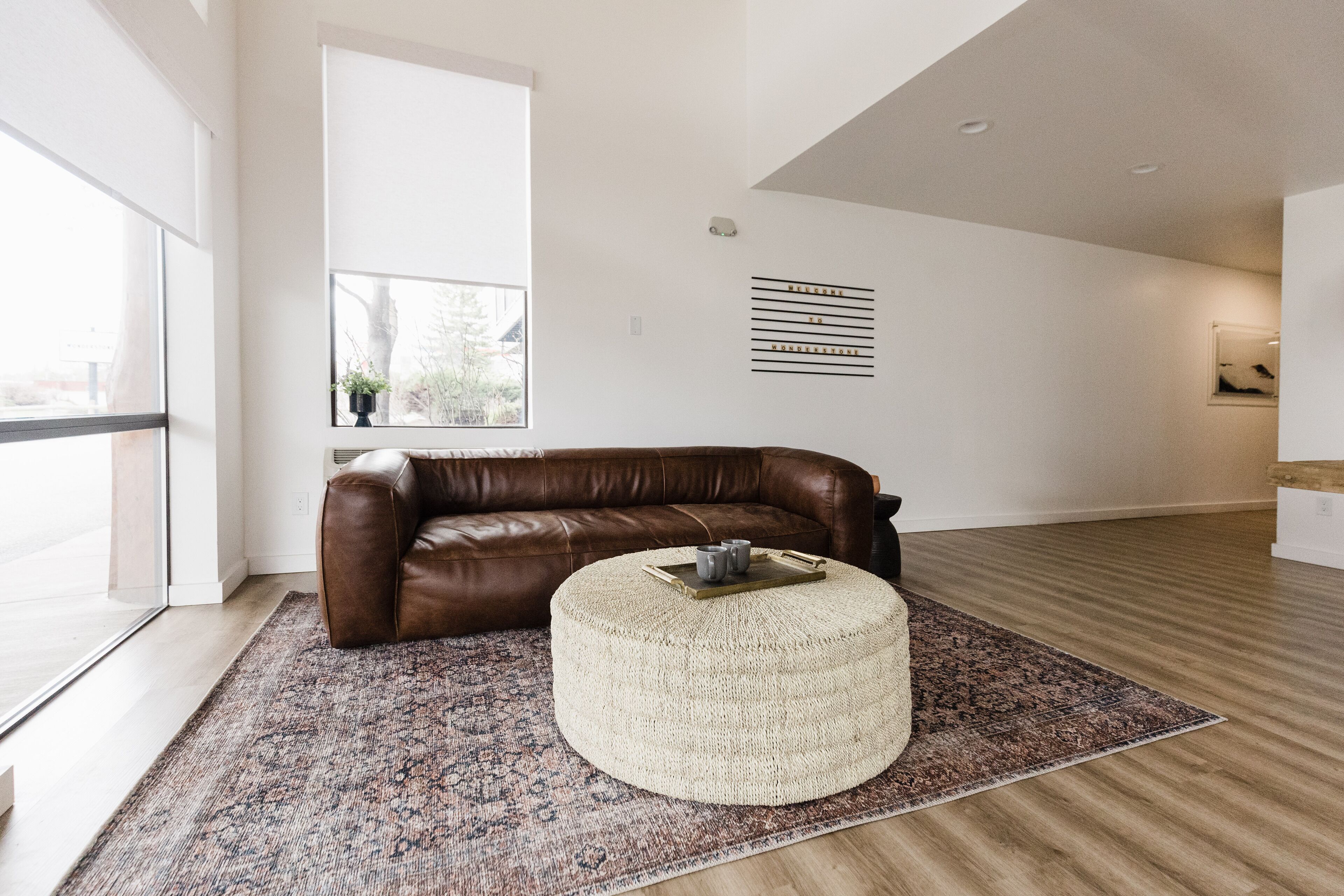 A modern living room with a brown leather sofa, a round ottoman, and a patterned rug.