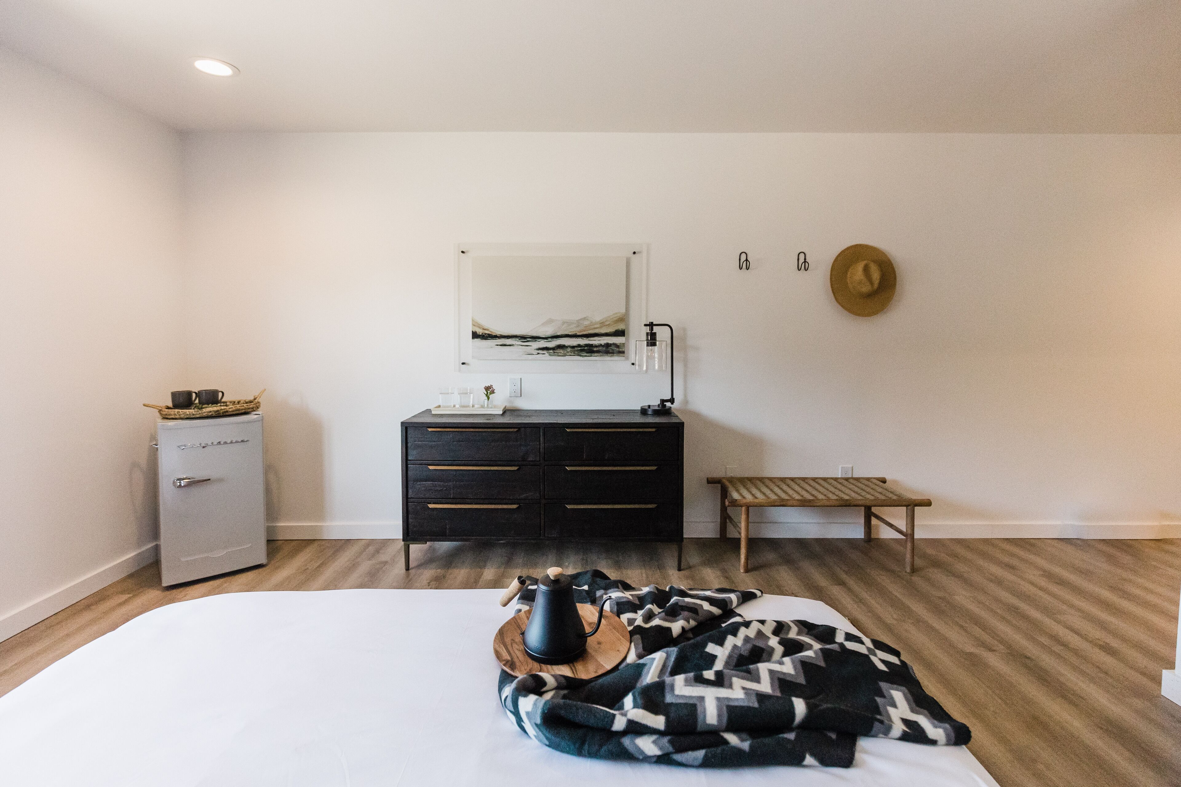 A bedroom with a bed, a dresser, a bench, a radiator, and a wall-mounted picture.