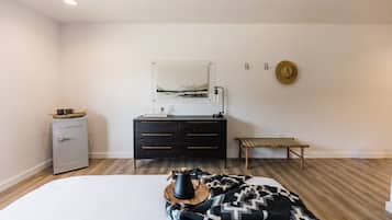 Un dormitorio con cama, cómoda, banqueta, radiador y un cuadro en la pared.
