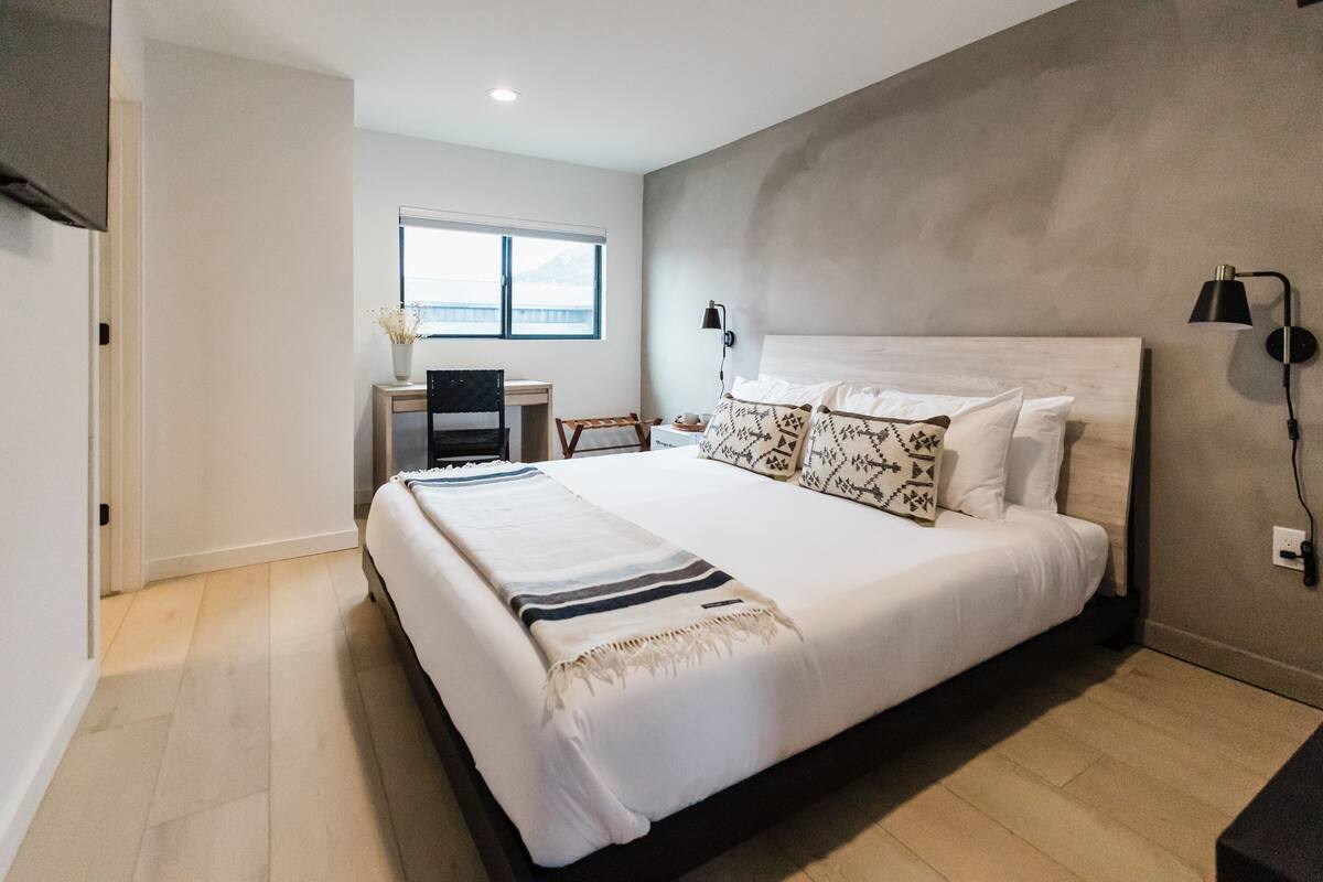 A modern bedroom with a large bed, a desk, and a window with a view.