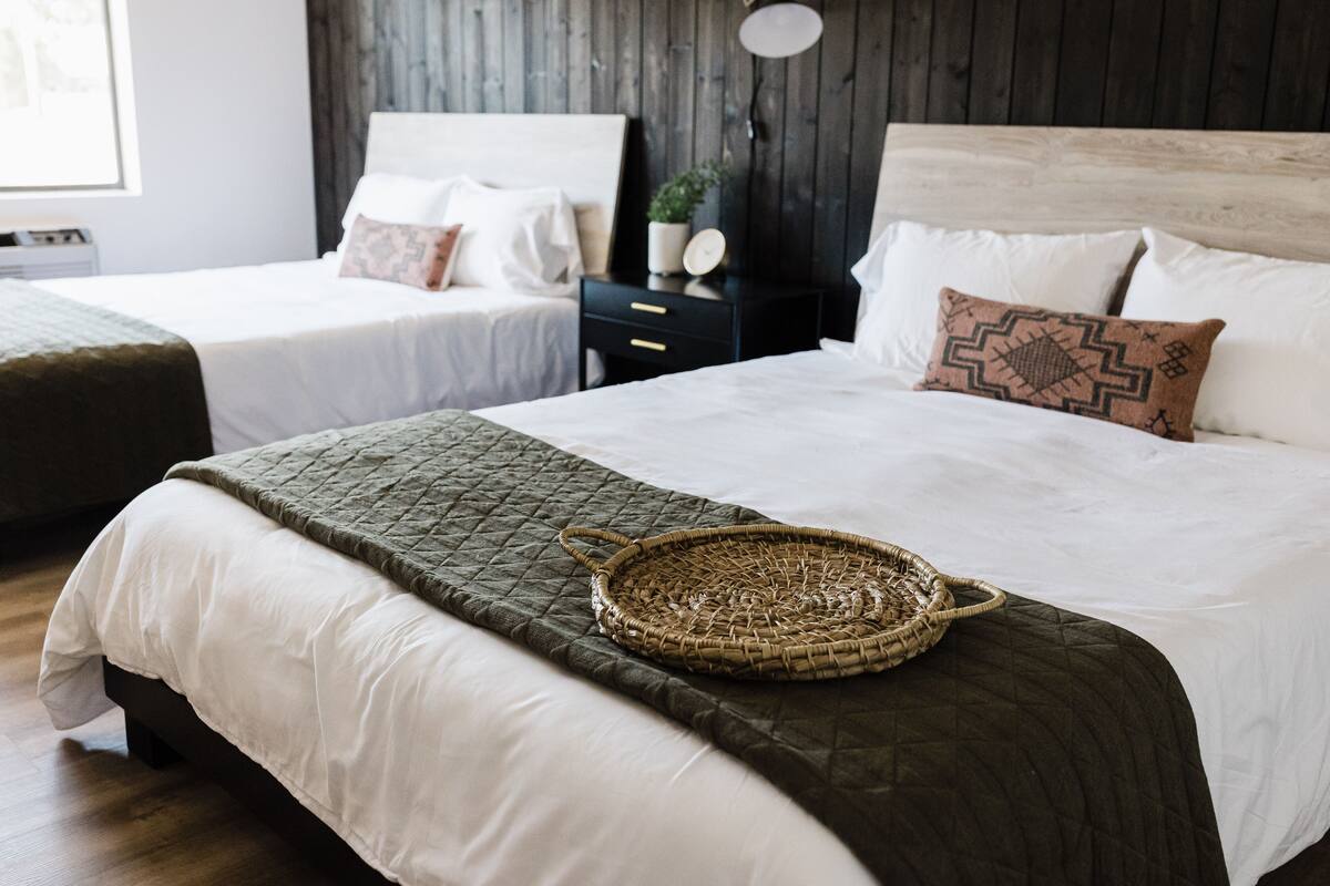A bedroom with two beds, dark wooden headboards, and a woven basket on the bed.