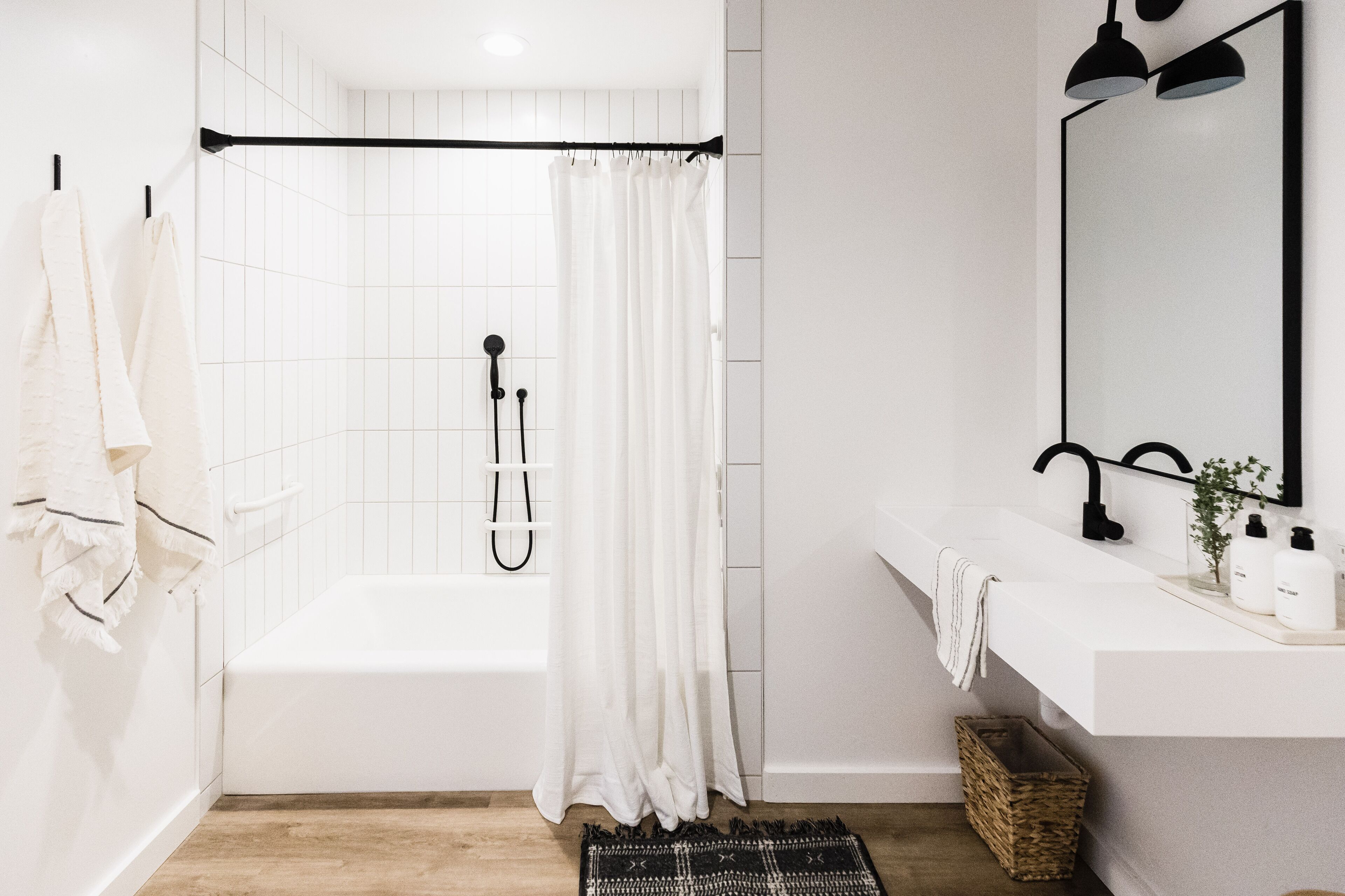 Un baño moderno con una bañera blanca, una cortina de ducha, un lavabo con espejo y una pequeña planta en el mostrador.