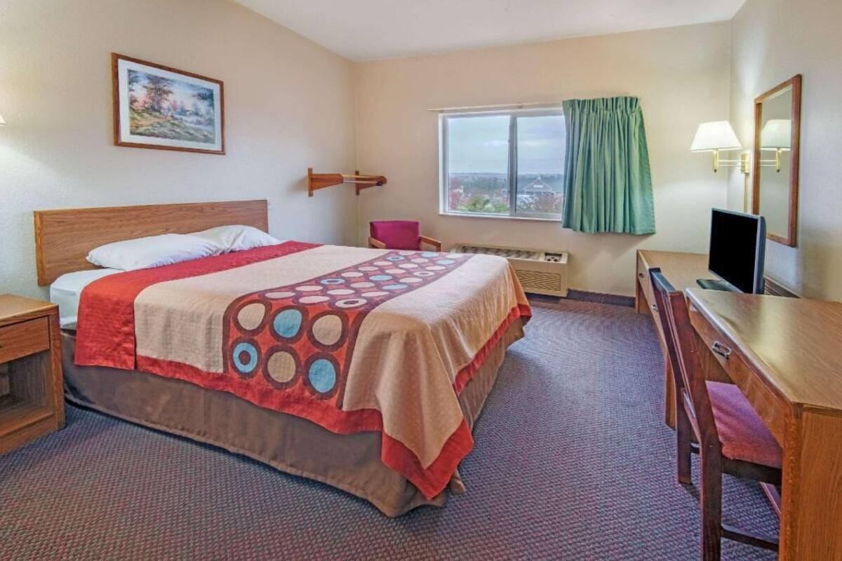 Une chambre d’hôtel avec un lit, un bureau, une chaise, une fenêtre donnant sur un beau paysage et un tableau accroché au mur.