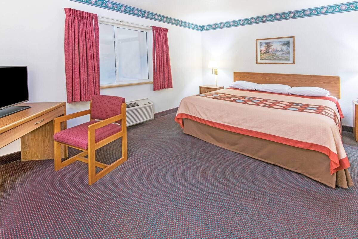 Une chambre d’hôtel comprenant un lit, un bureau avec une chaise, une télévision et une fenêtre avec des rideaux.