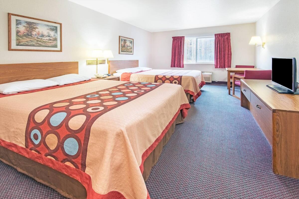 Une chambre d’hôtel avec deux lits, un bureau, une chaise, une télévision et des œuvres d’art accrochées aux murs.