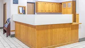 Una recepción con encimera de madera, un certificado enmarcado en la barra y un cartel que anuncia servicios como desayuno gratuito y Wi-Fi.
